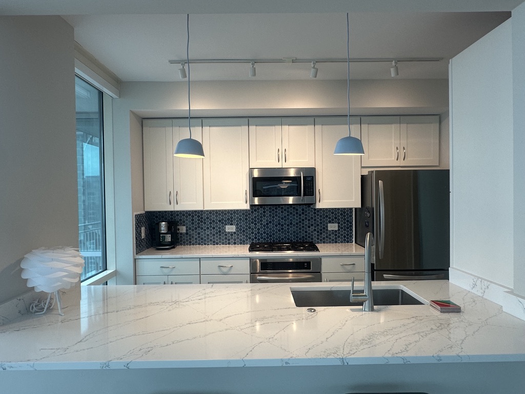 Modern kitchen with white cabinets, marble waterfall island, and blue mosaic backsplash